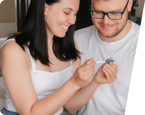 A couple looking down and smiling at the results of a pregnancy test